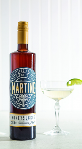 brown bottle with gold top and turquoise label reading Martine on the left. On the right is a coup glass filled with slightly yellow liquid with a lime wedge on the rim. 