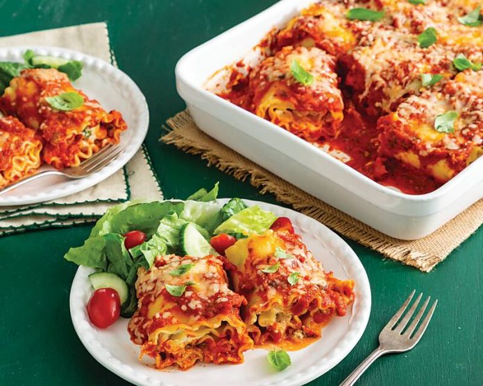 Chicken-Goat Cheese-Mustard Green Lasagna Roll-Ups in white casserole dish, two servings on white plates nearby